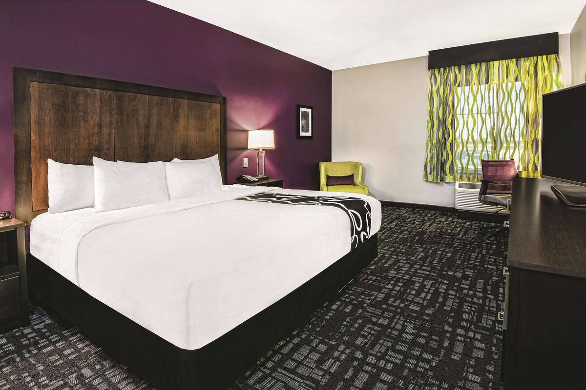 A hotel room with a large bed, a desk, a chair, a lamp, and a TV.