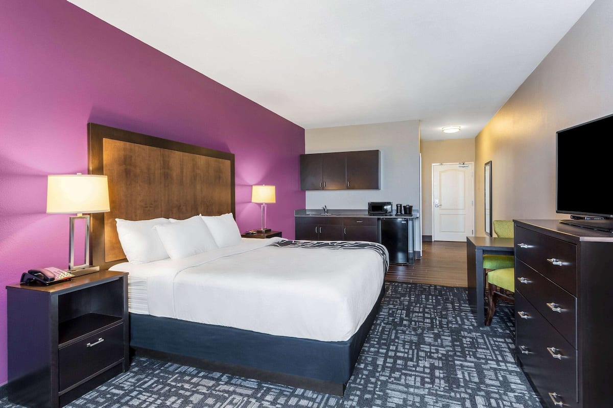 A hotel room with a bed, bedside tables, a desk, a TV, and a kitchenette.
