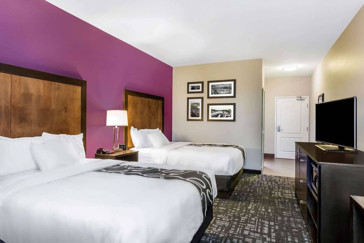 A hotel room with two beds, a TV, a desk, and a door.