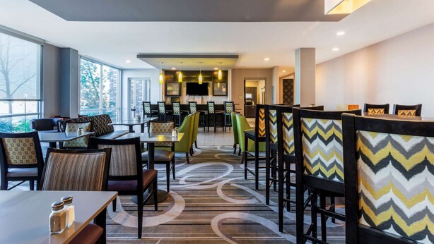 A modern dining area with multiple tables and chairs, large windows, and a patterned carpet. - La Quinta Inn & Suites by Wyndham Monahans (Monahans)