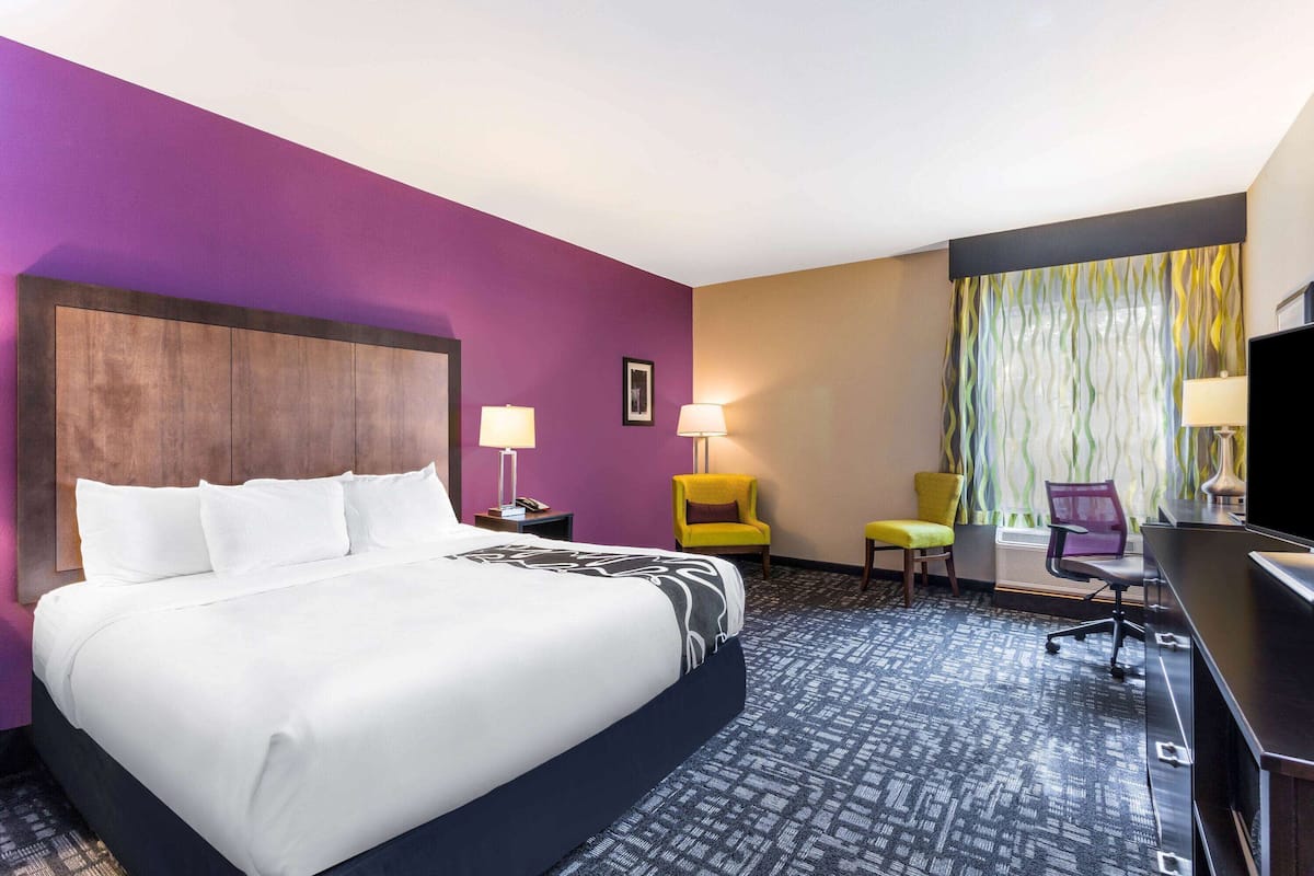 A hotel room with a large bed, two chairs, a desk, and a television.