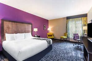 Une chambre d’hôtel avec un grand lit, deux fauteuils, un bureau et une télévision.