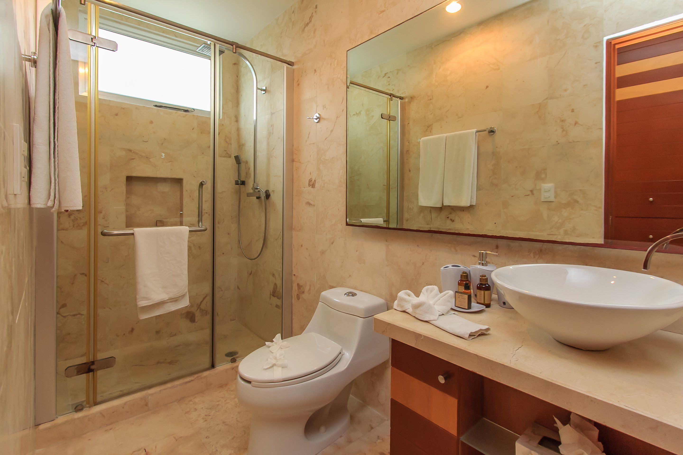 Un baño moderno con ducha envuelta en vidrio, inodoro blanco, lavabo grande y espejo sobre él.