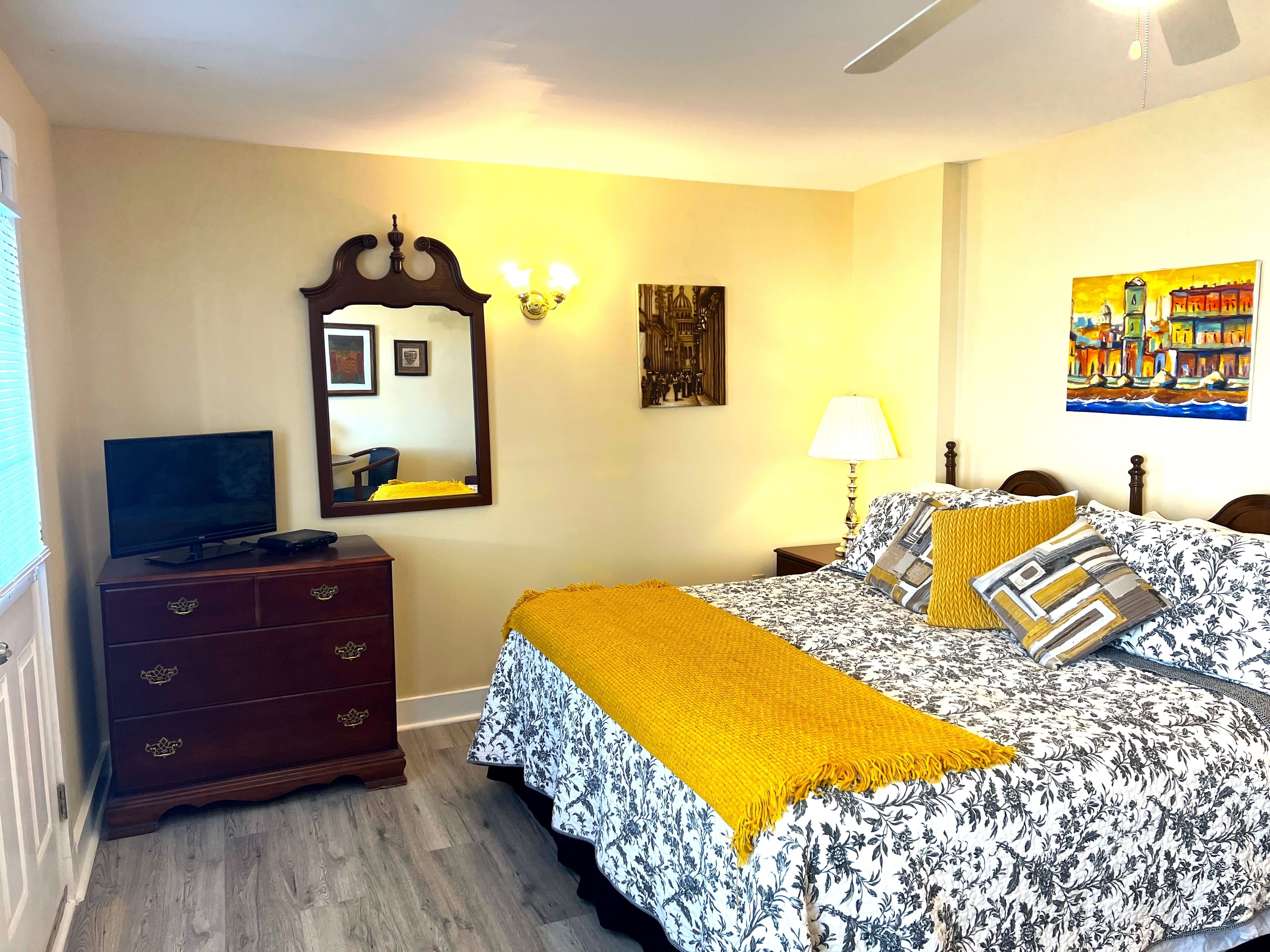 A bedroom with a bed, a dresser, a television, a mirror, and artwork on the walls.