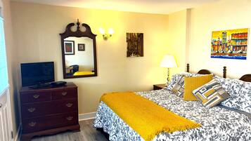 A bedroom with a bed, a dresser, a television, a mirror, and artwork on the walls.