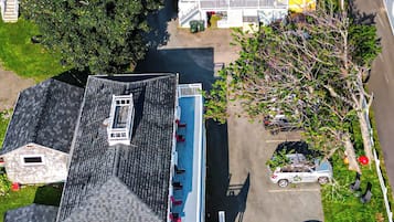 An aerial view of a residential area with houses, a swimming pool, and parked cars.