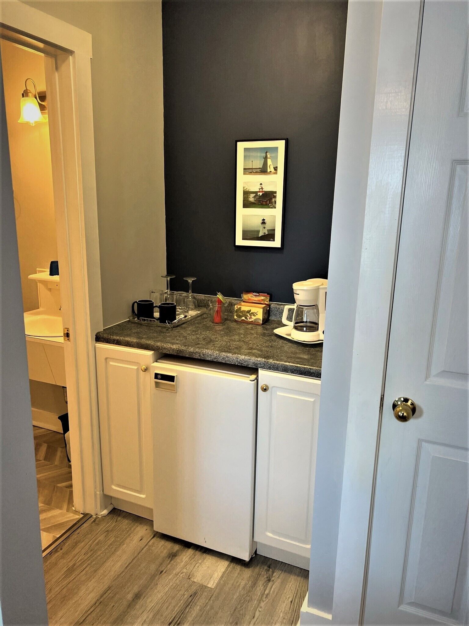 A compact kitchen with white cabinets, a granite countertop, and a dark wall.