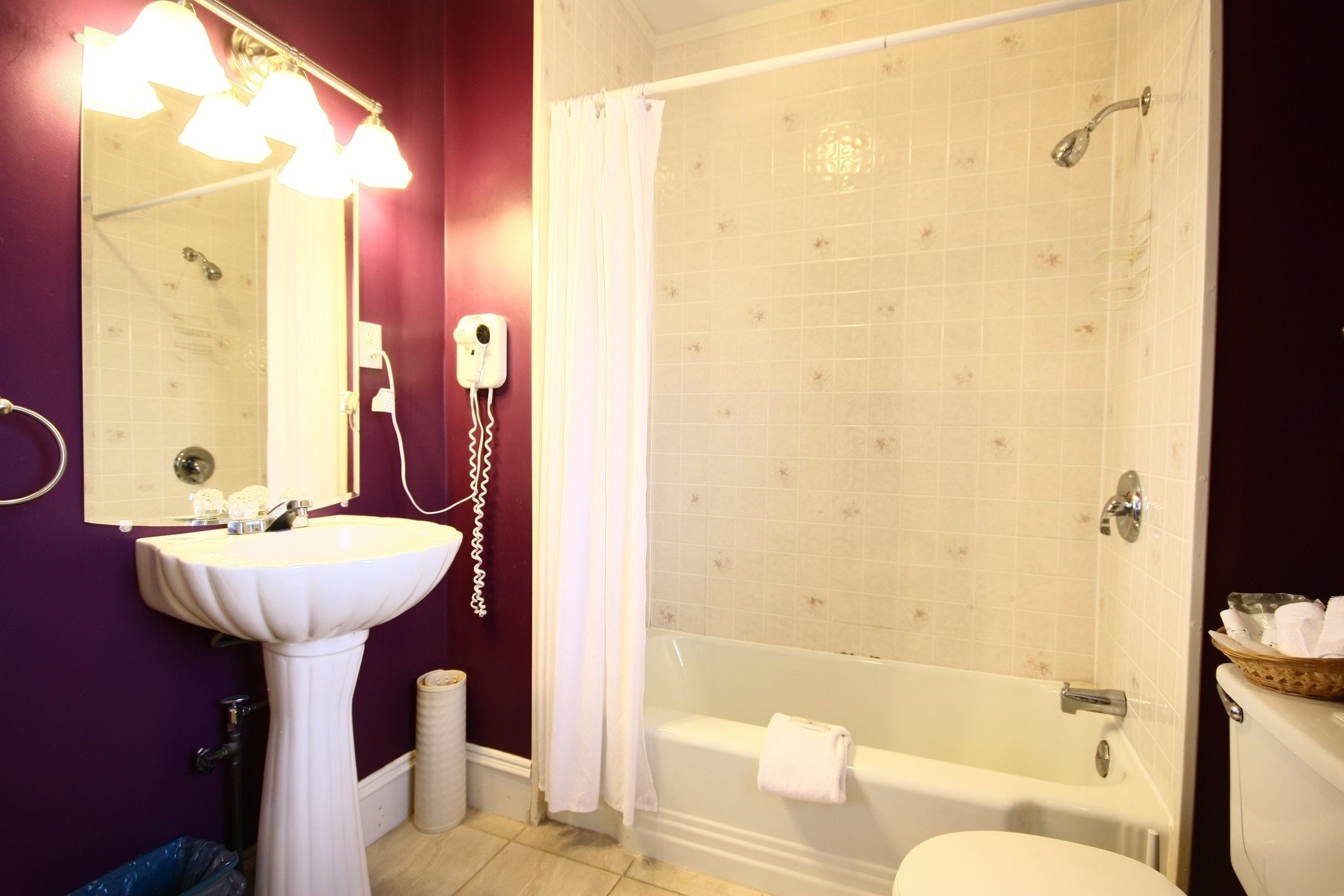 A bathroom with a pedestal sink, a mirror with lights, a shower, and a bathtub.
