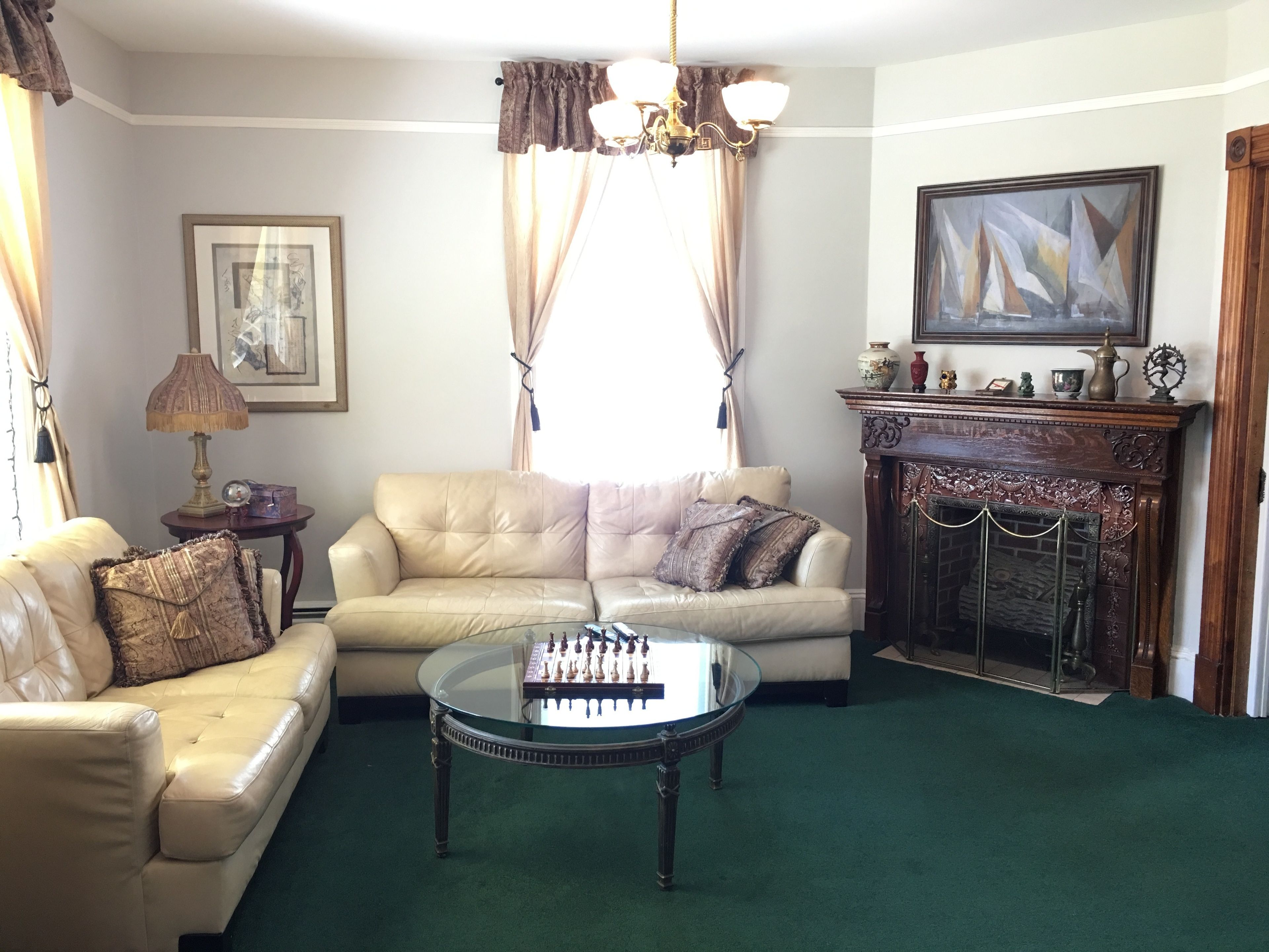 Un salón con un sofá color beige, una mesa de centro de vidrio con piezas de ajedrez, una chimenea y un cuadro en la pared.