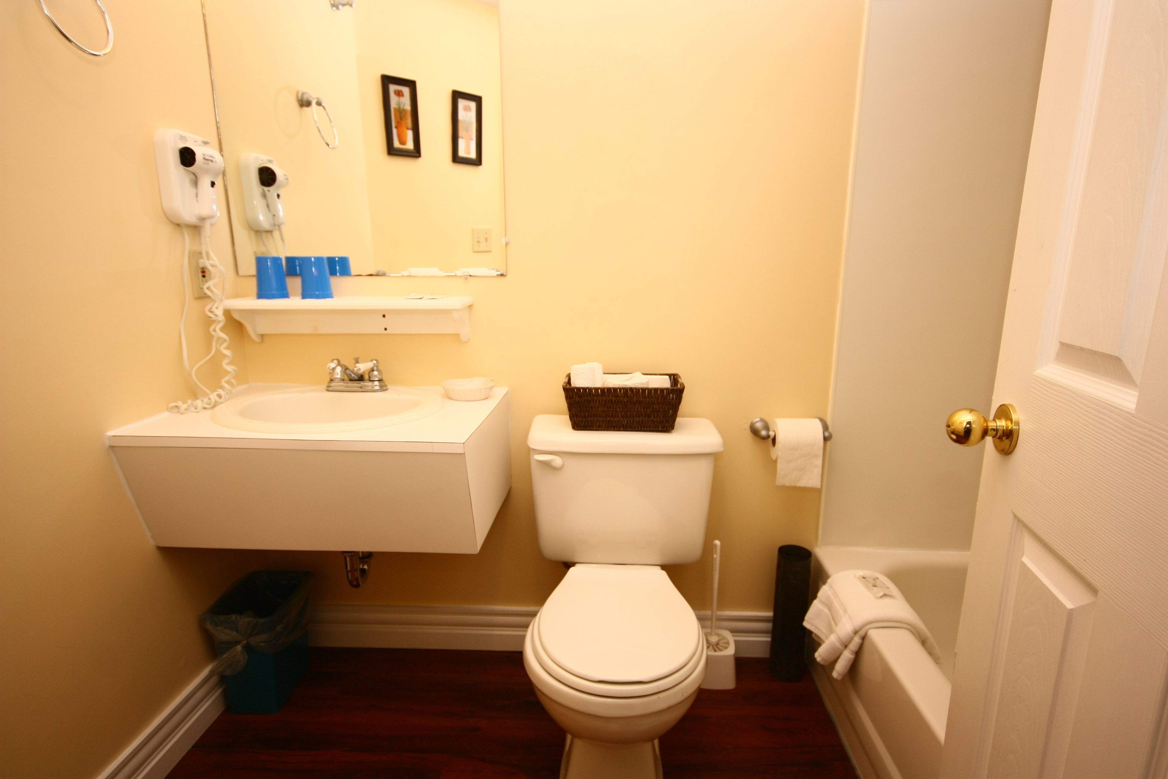 A bathroom with a white sink, toilet, and bathtub. There is a trash can and a basket on the toilet.