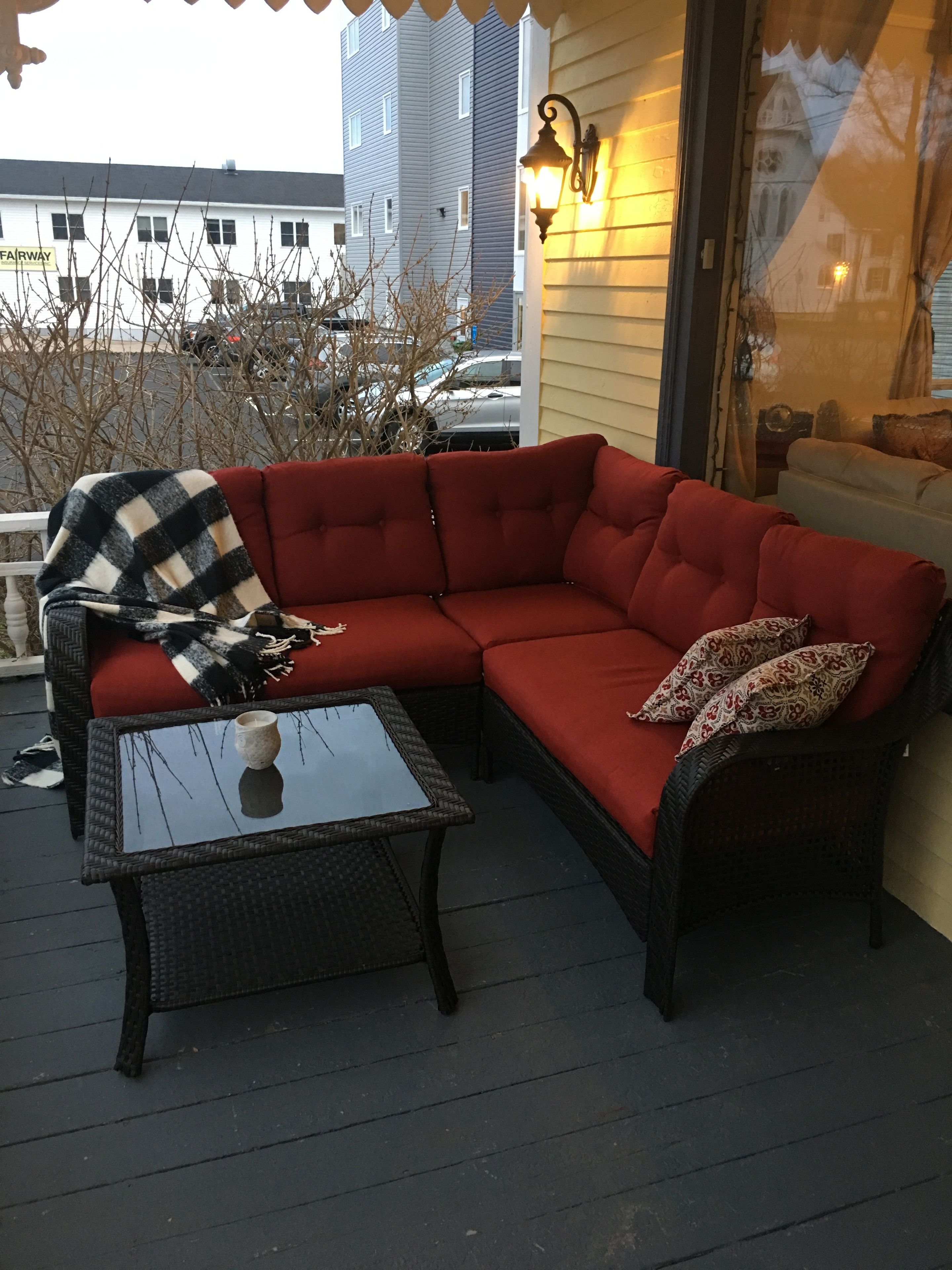 Un sofá modular rojo con una manta de cuadros blancos y negros, una mesa de centro con superficie de vidrio y almohadones estampados.
