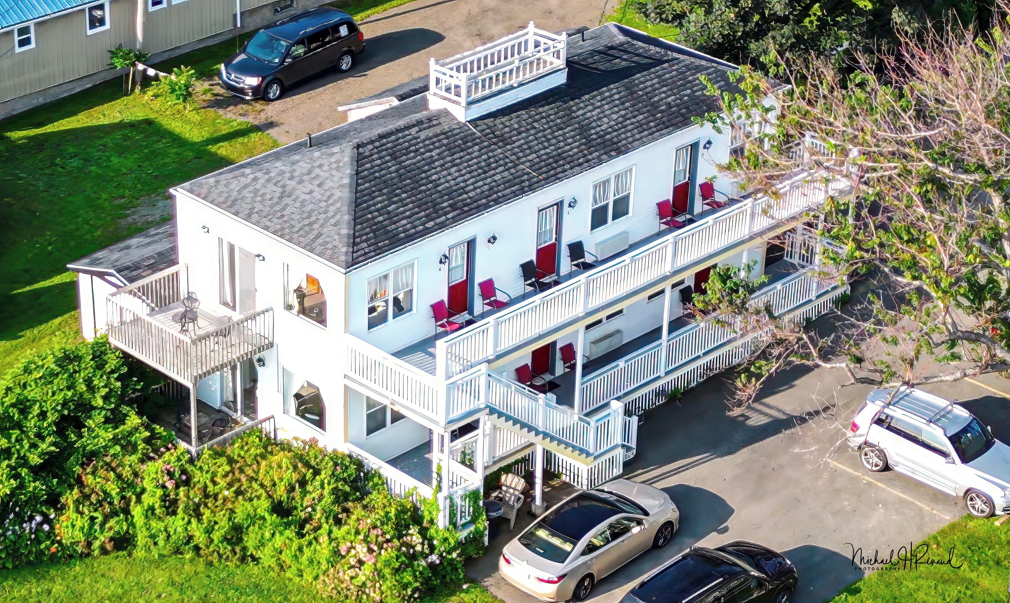 A multi-story building with balconies, a covered front porch, and a parking area.