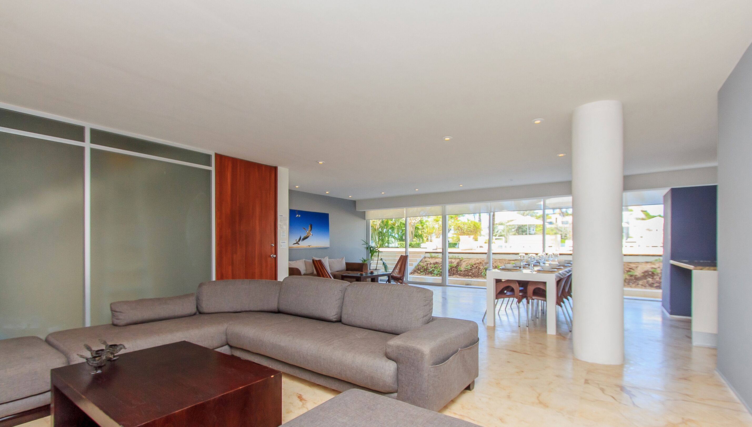 A modern living room with a sectional sofa, a wooden coffee table, and a dining area with a table set for four.