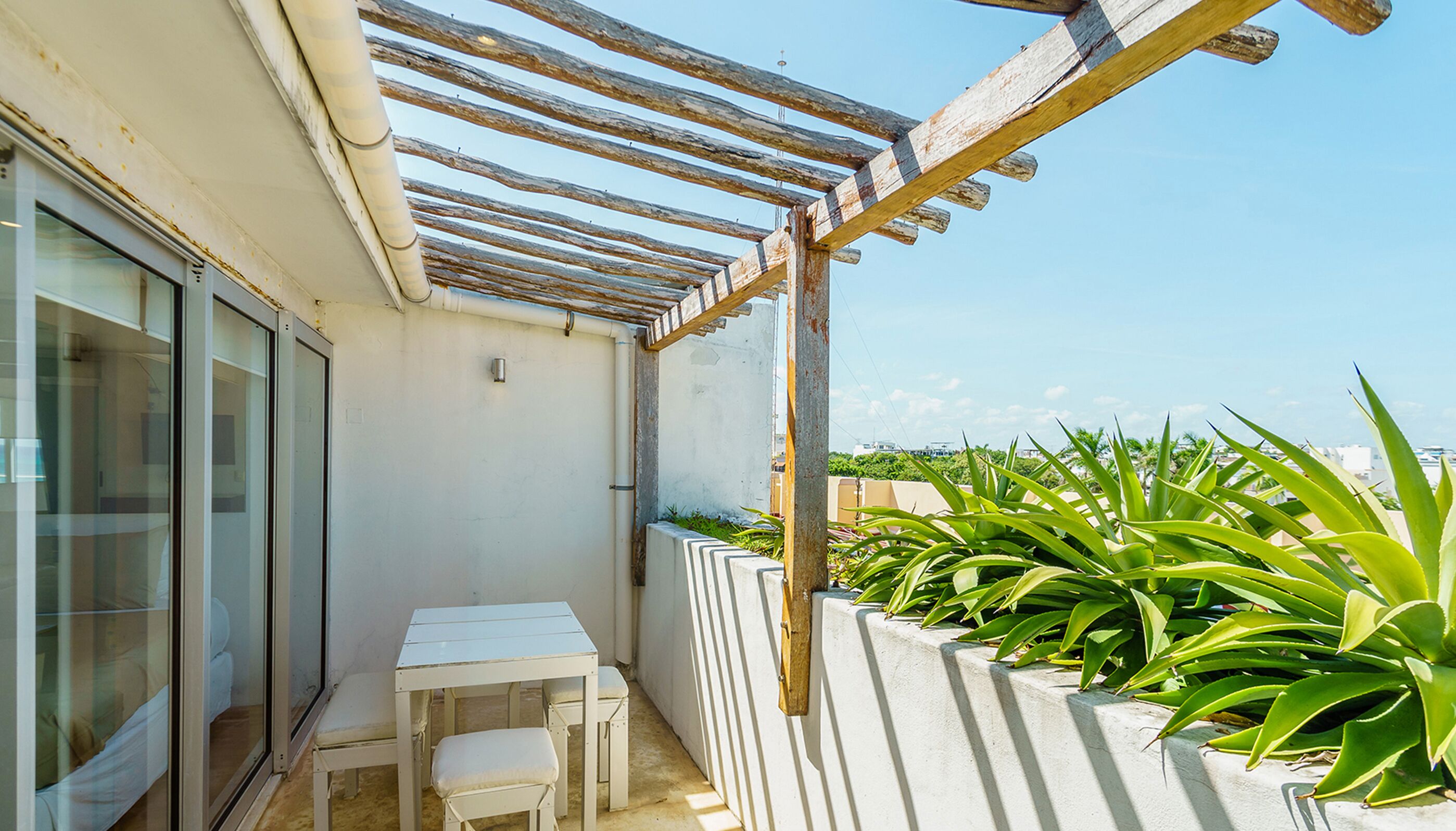 Un balcon agrémenté d’une pergola, d’une table, de deux chaises et de plantes en pot.