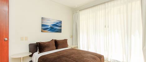 Un dormitorio con una cama, un cuadro, una ventana con cortinas y una puerta.
