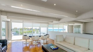 A spacious living area with a large window overlooking a scenic view, a white sofa, and a round table with chairs. - MAGIA by Stella Rentals (Playa del Carmen)