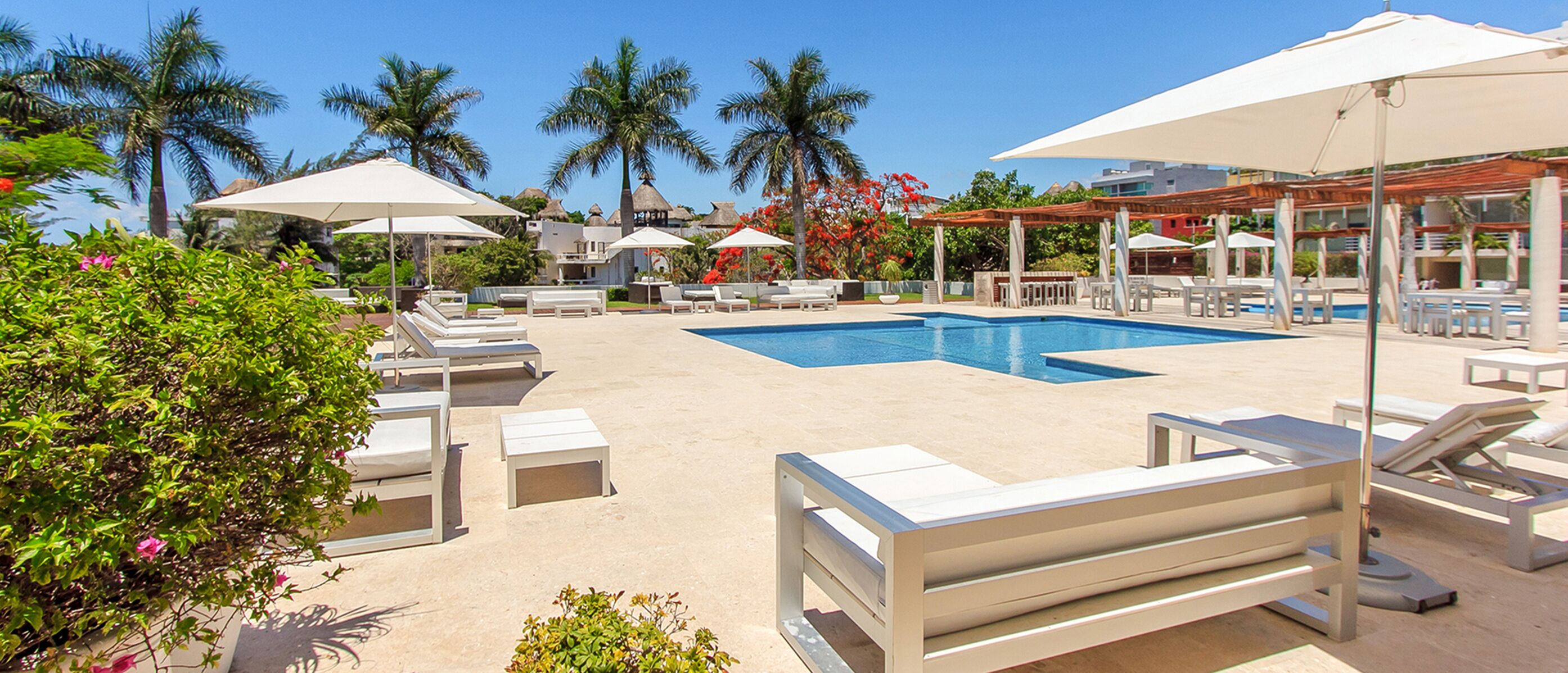 Un área junto a la piscina con sillones, sombrillas y una piscina azul cristalina.