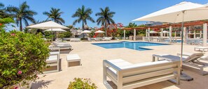 Un espace aménagé au bord de la piscine, avec des chaises longues, des parasols et une piscine à l’eau d’un bleu limpide.
