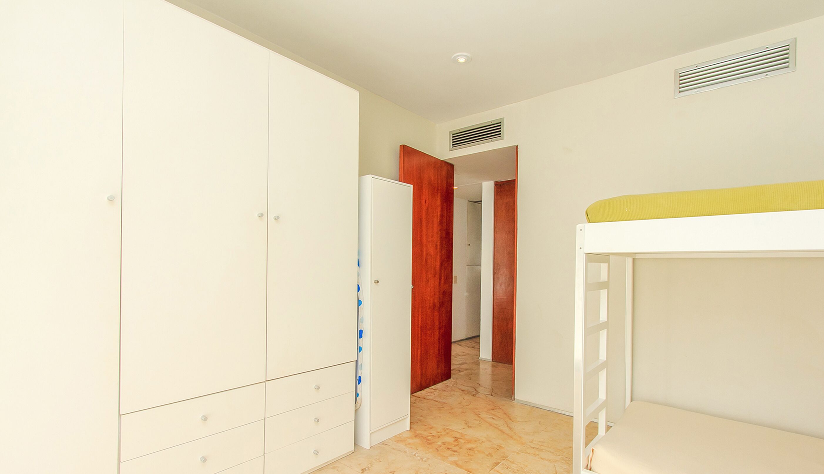 A narrow hallway with a white wardrobe, a wooden door, and a bunk bed.