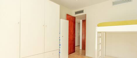 A narrow hallway with a white wardrobe, a wooden door, and a bunk bed.