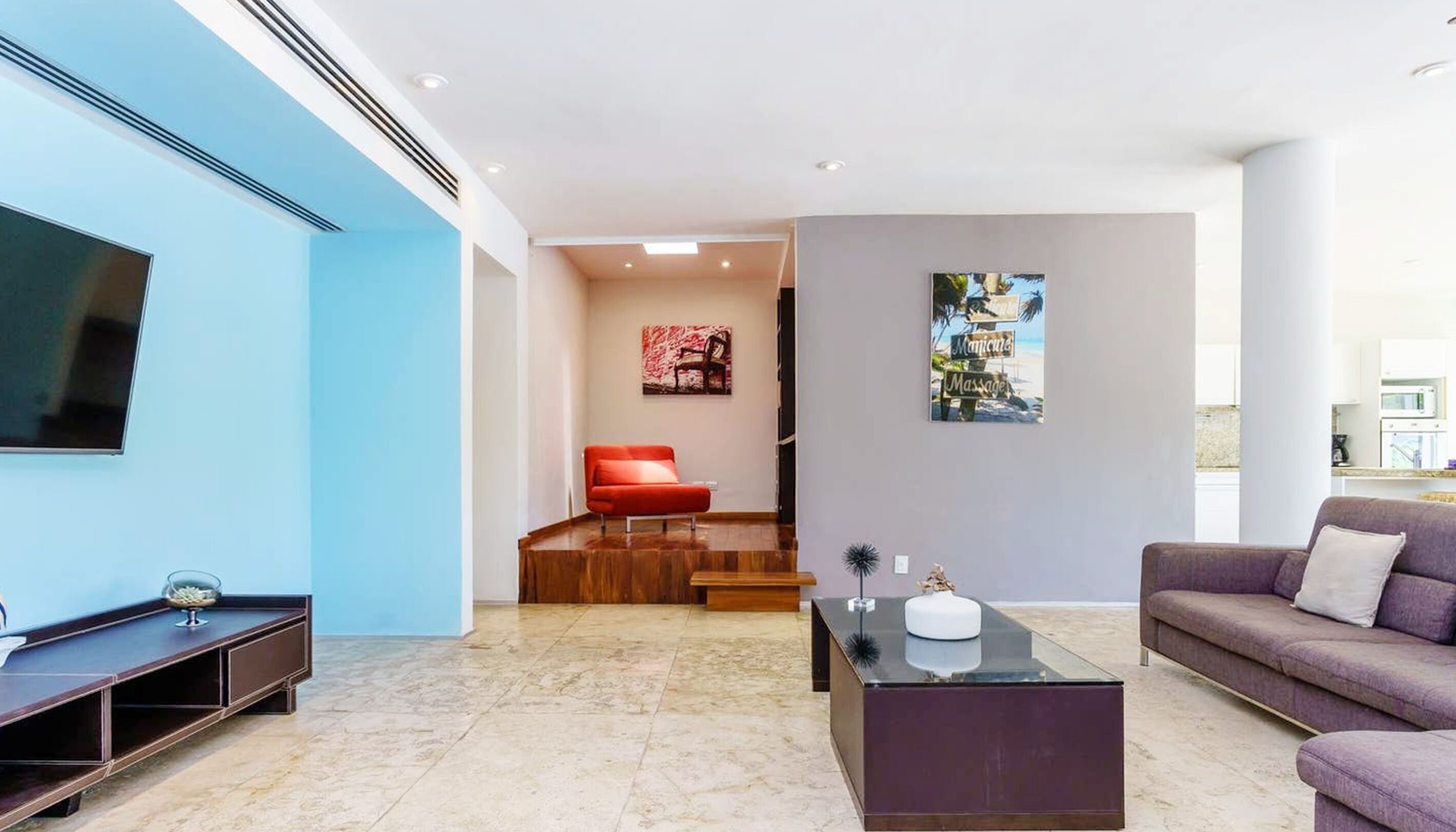 Una sala moderna con un televisor de pantalla plana, una silla roja, un sofá púrpura y una mesa de centro de vidrio.