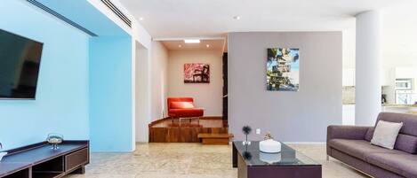 Una sala moderna con un televisor de pantalla plana, una silla roja, un sofá púrpura y una mesa de centro de vidrio.