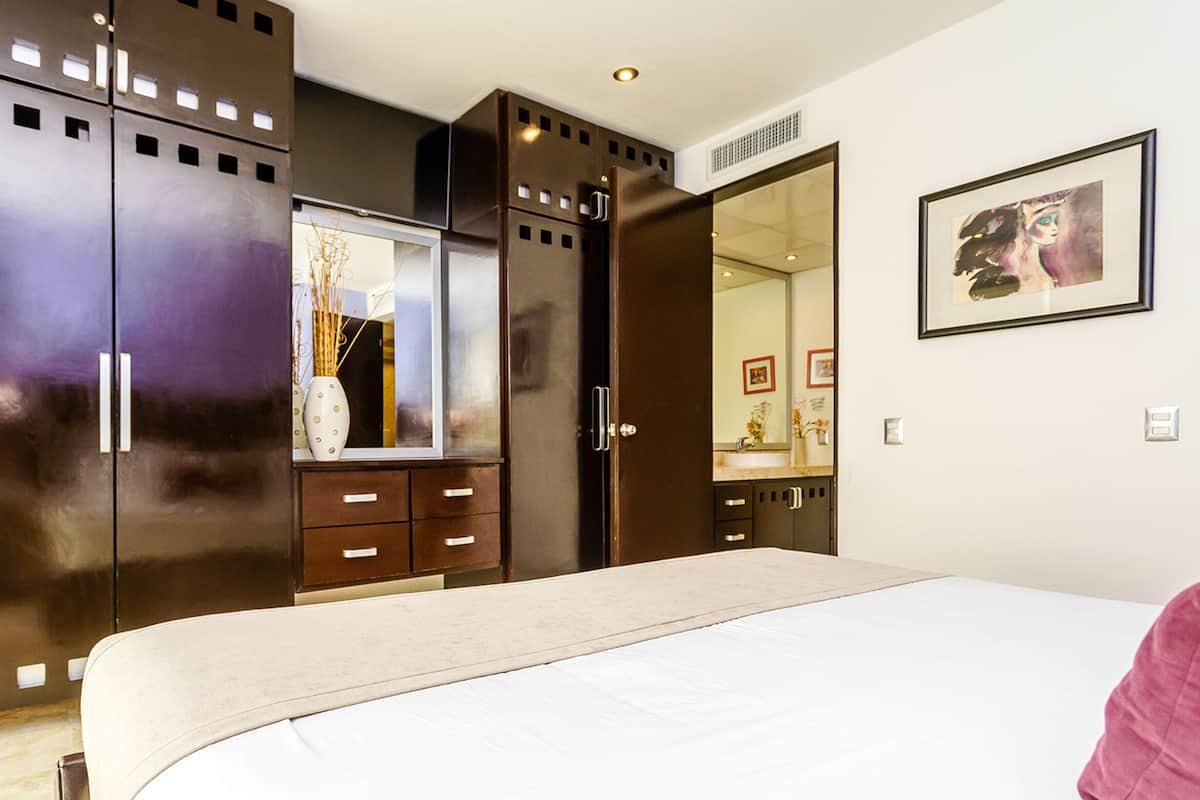 Une chambre à coucher avec un lit, une armoire, un miroir et un tableau accroché au mur.