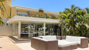 An outdoor seating area with a glass enclosure, a large sectional sofa, and a wooden deck. - MAGIA by Stella Rentals (Playa del Carmen)