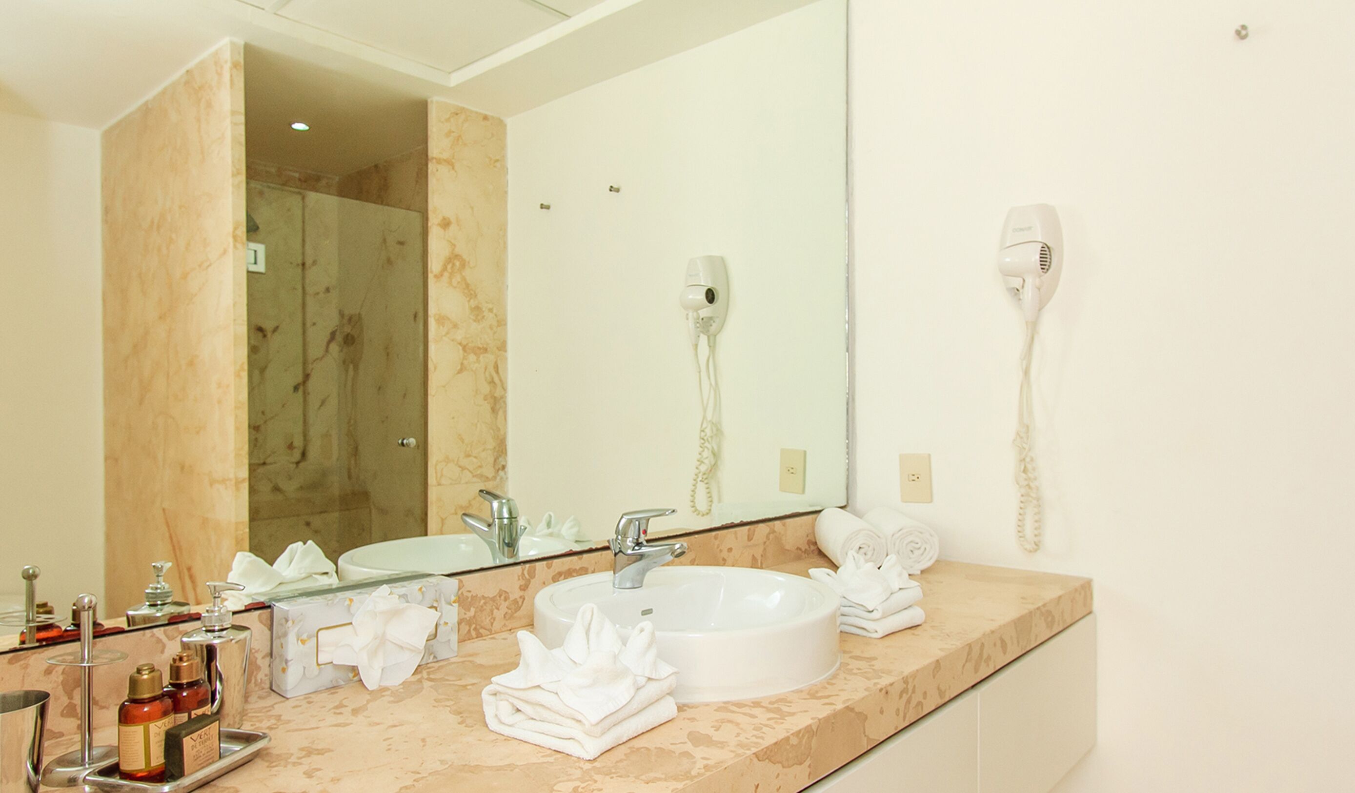 A bathroom with a marble countertop, a sink, a mirror, a hairdryer, and a towel rack.