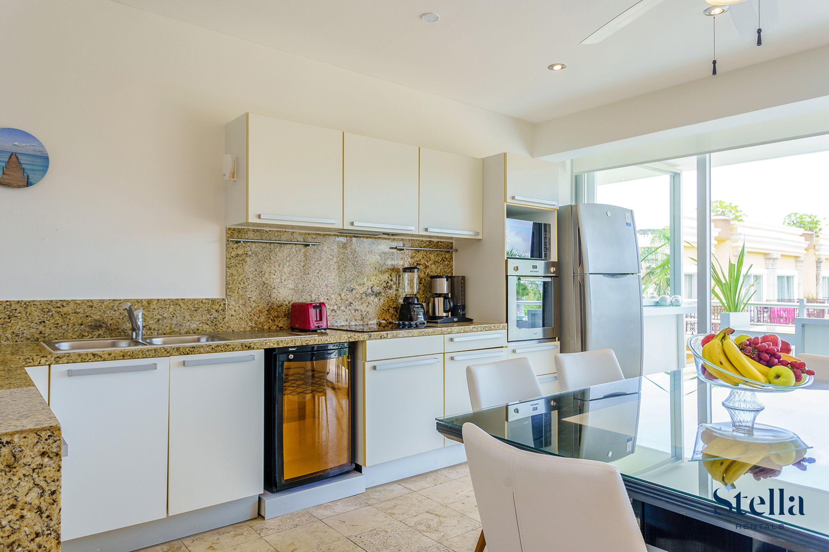 A modern kitchen with white cabinets, granite countertops, a dishwasher, and a dining area with a glass table and chairs.