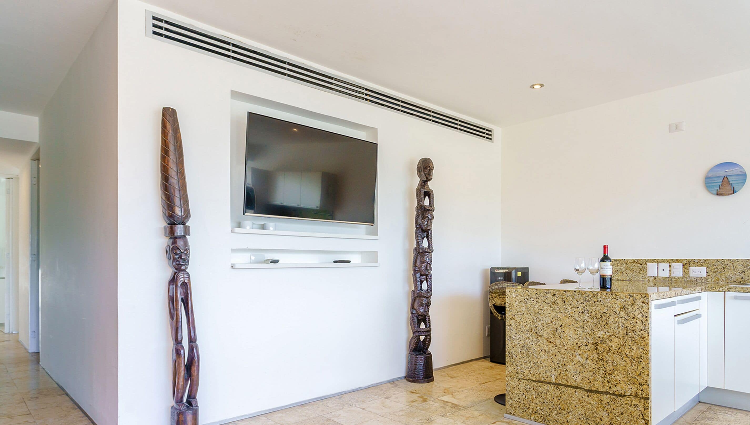 A modern kitchen with a built-in TV, granite countertops, and a small island with wine glasses.