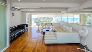 A spacious living room with a black leather sofa, a white sofa, and a coffee table. There is a large window with a view of the ocean. - MAGIA by Stella Rentals (Playa del Carmen)