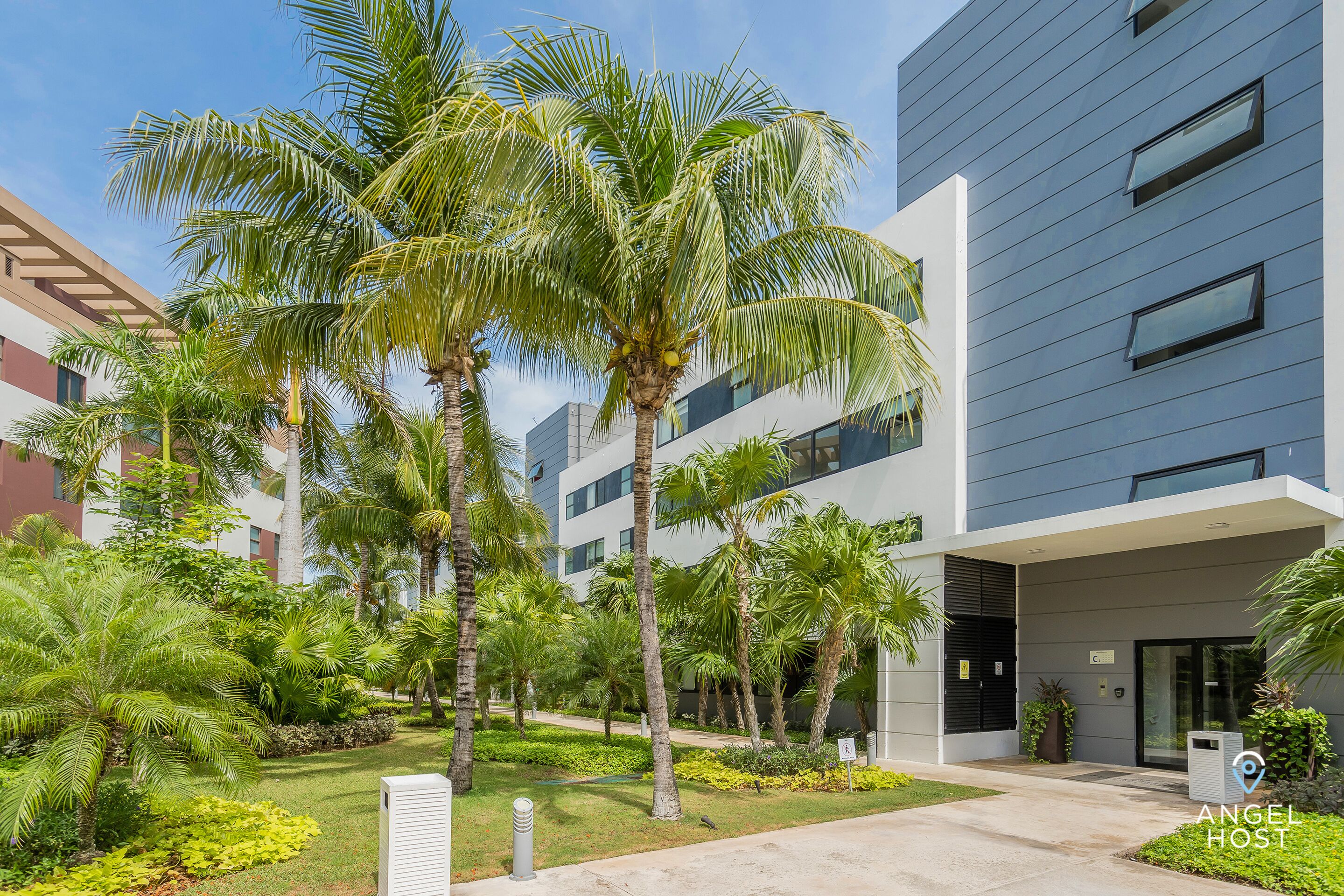 Un edificio moderno con techo plano, ventanas amplias y un jardín bien cuidado con palmeras.