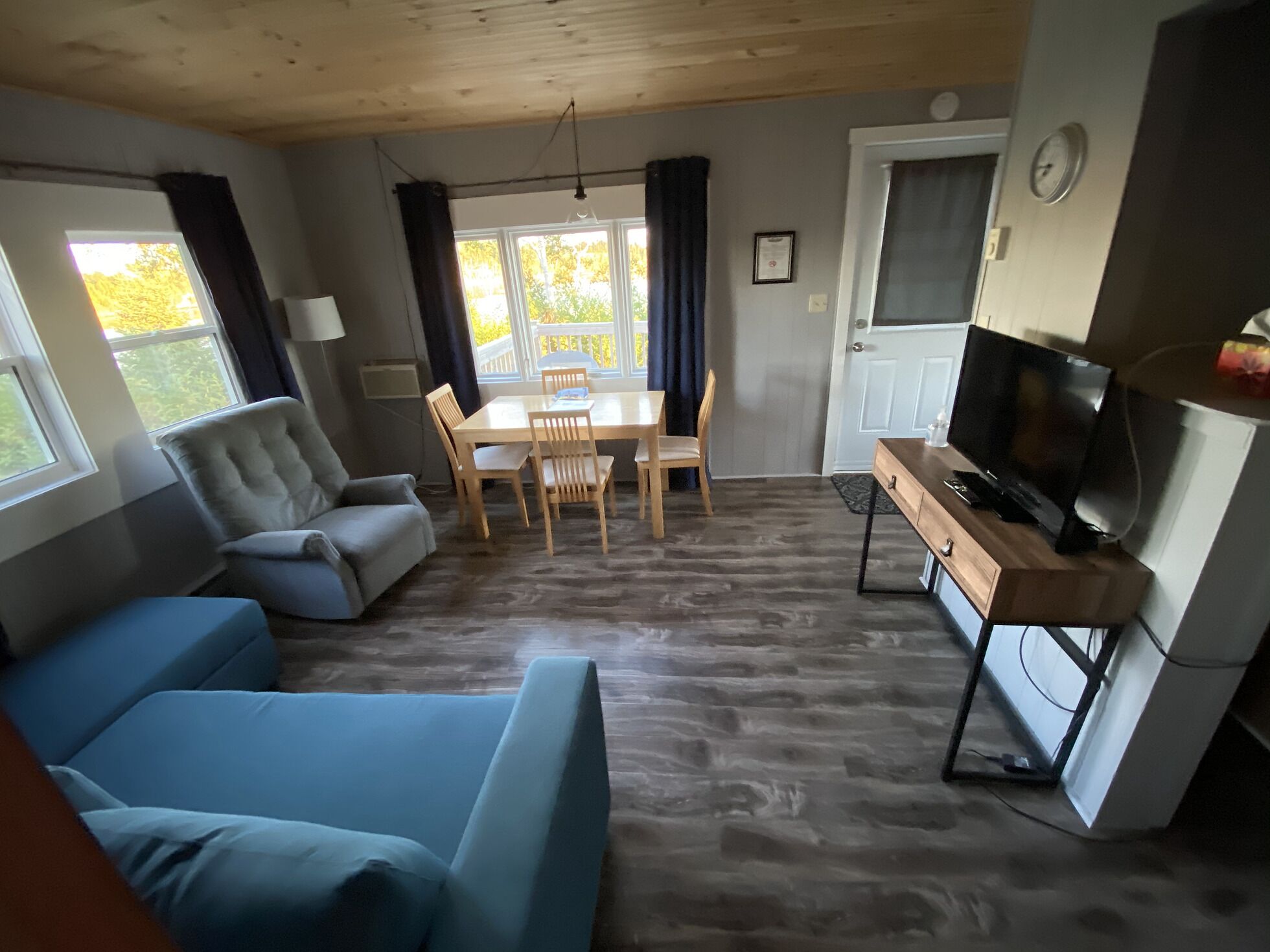 A compact living space with a sofa, a dining table with chairs, a TV, and a small kitchenette.