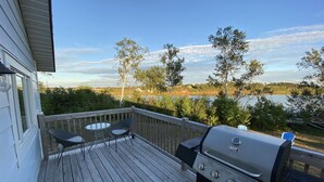 Une terrasse avec un barbecue et deux chaises, offrant une vue sur un lac et des arbres.