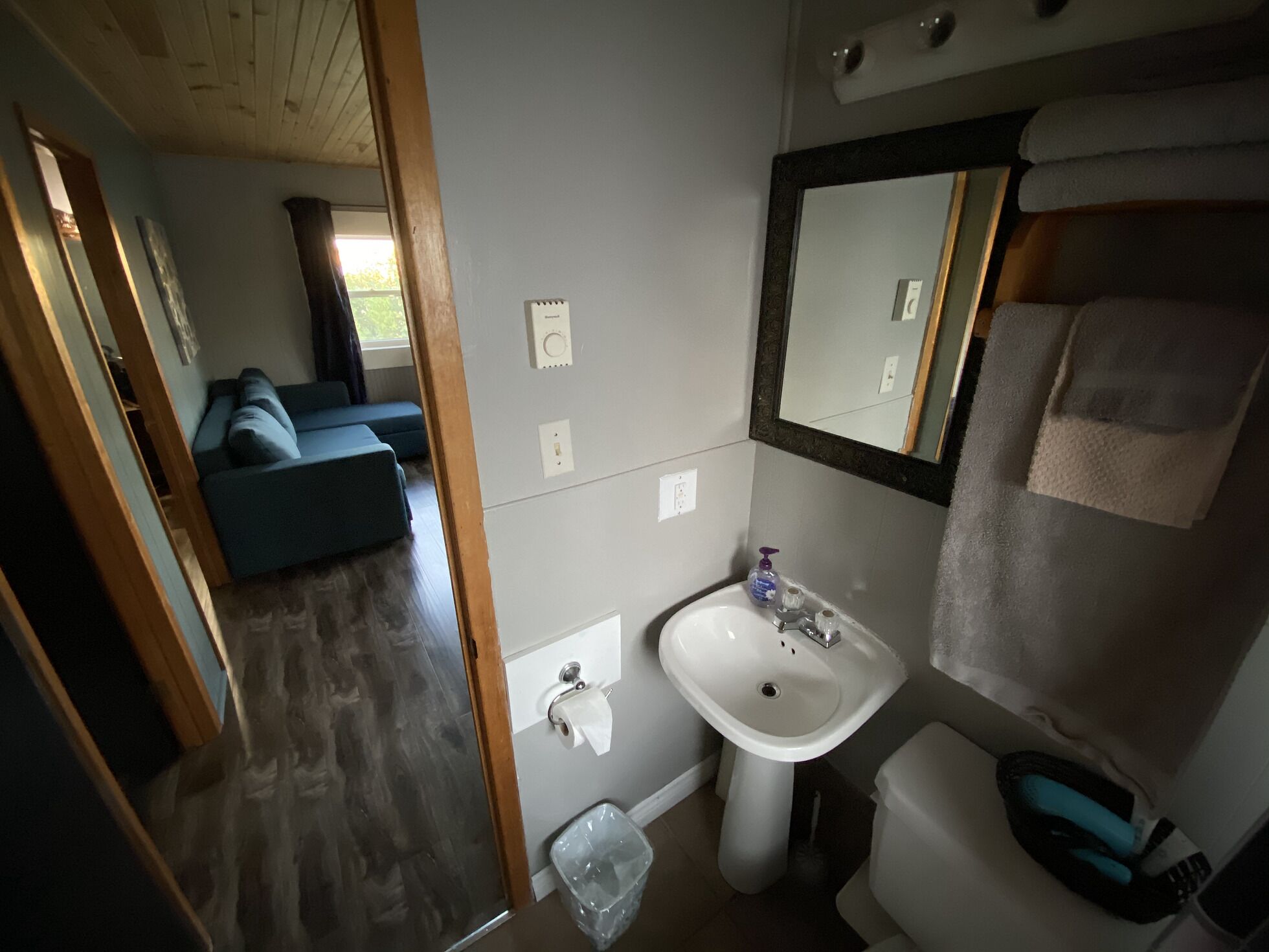 A compact bathroom with a sink, mirror, and toilet. A small trash bin is visible.