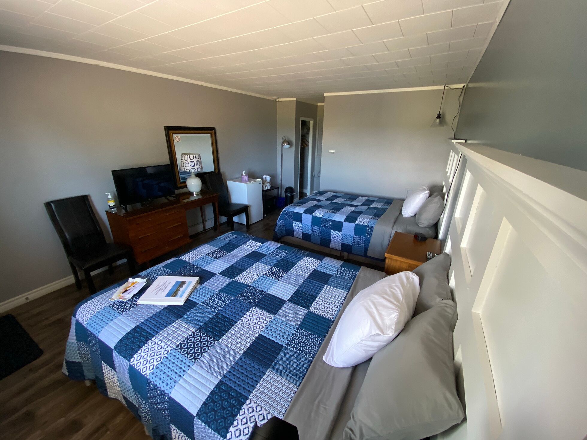 Habitación de hotel con dos camas, un escritorio, una silla, un televisor y una kitchenette pequeña.
