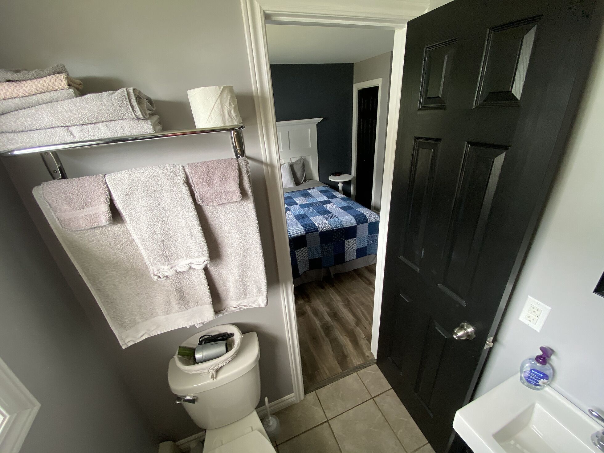 A bathroom with a toilet, a towel rack with multiple towels, a sink, and a door leading to another room.