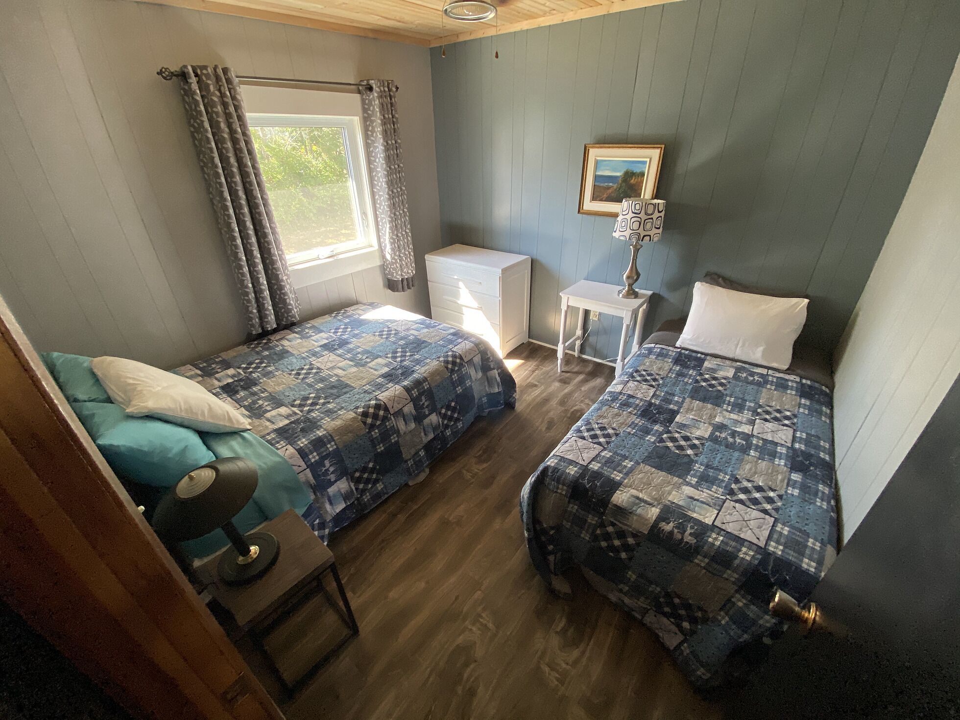 Un dormitorio con dos camas, una mesita, una lámpara y un ventanal con cortinas.