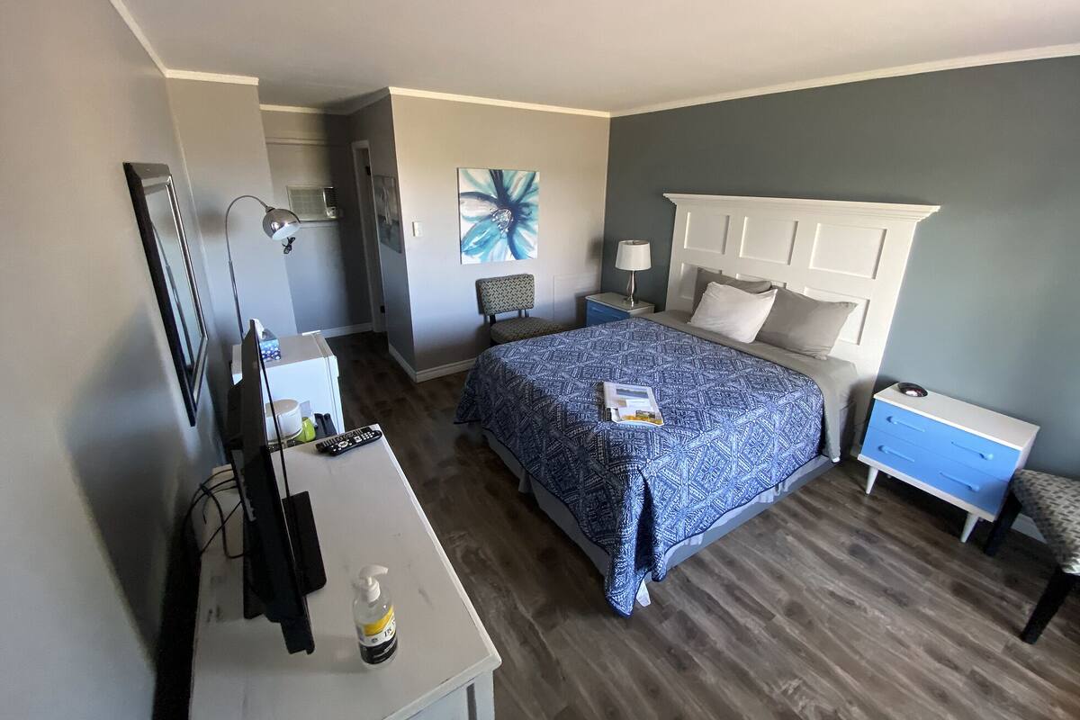 Habitación de hotel con cama, mesitas de noche, escritorio, silla, lámpara y un cuadro en la pared.