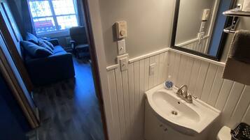 A bathroom with a sink, toilet, and mirror. There is a window with a view of the outside.