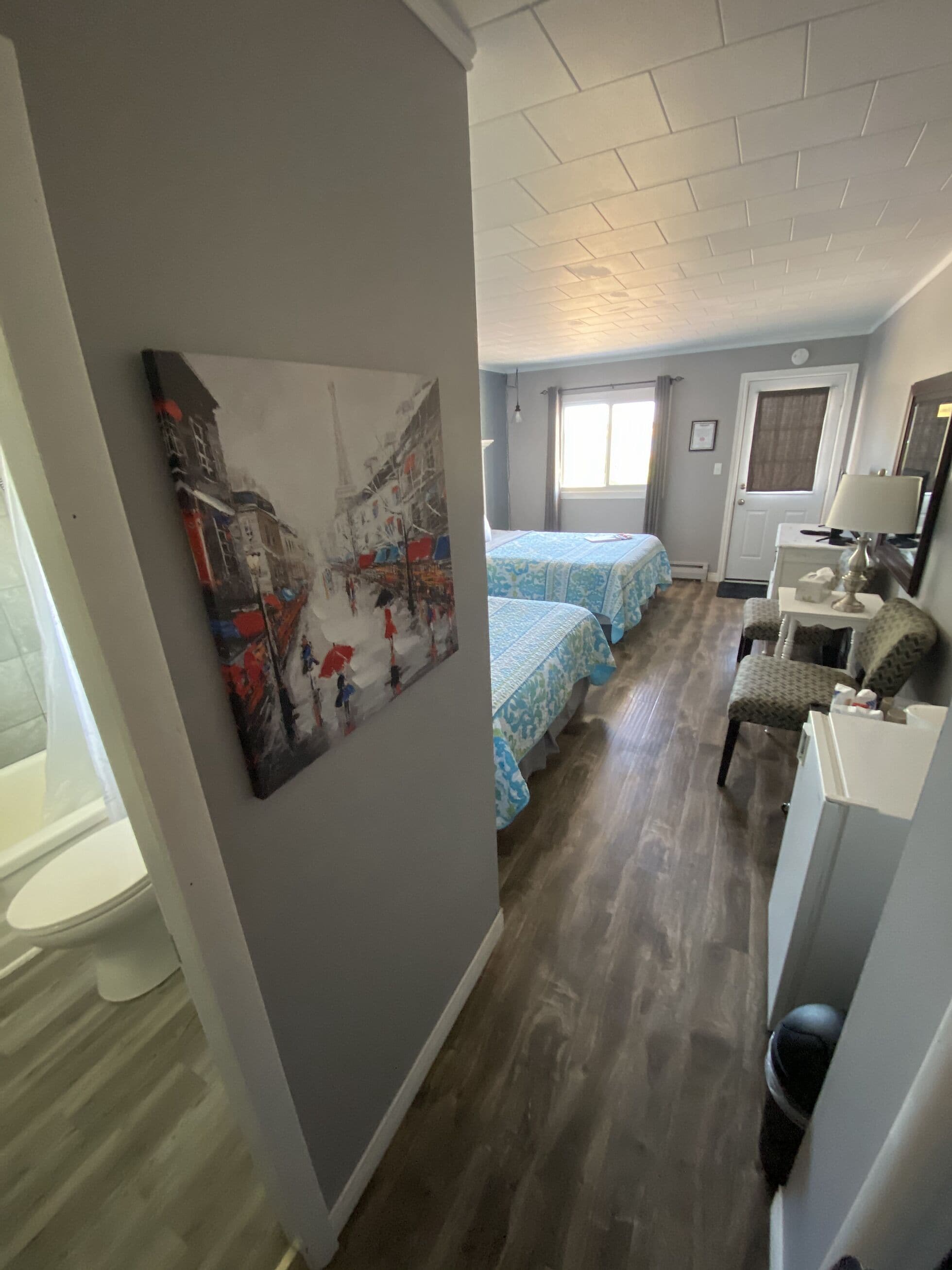 Una camera d'albergo con un letto, una scrivania, una sedia, un quadro appeso al muro e una finestra.