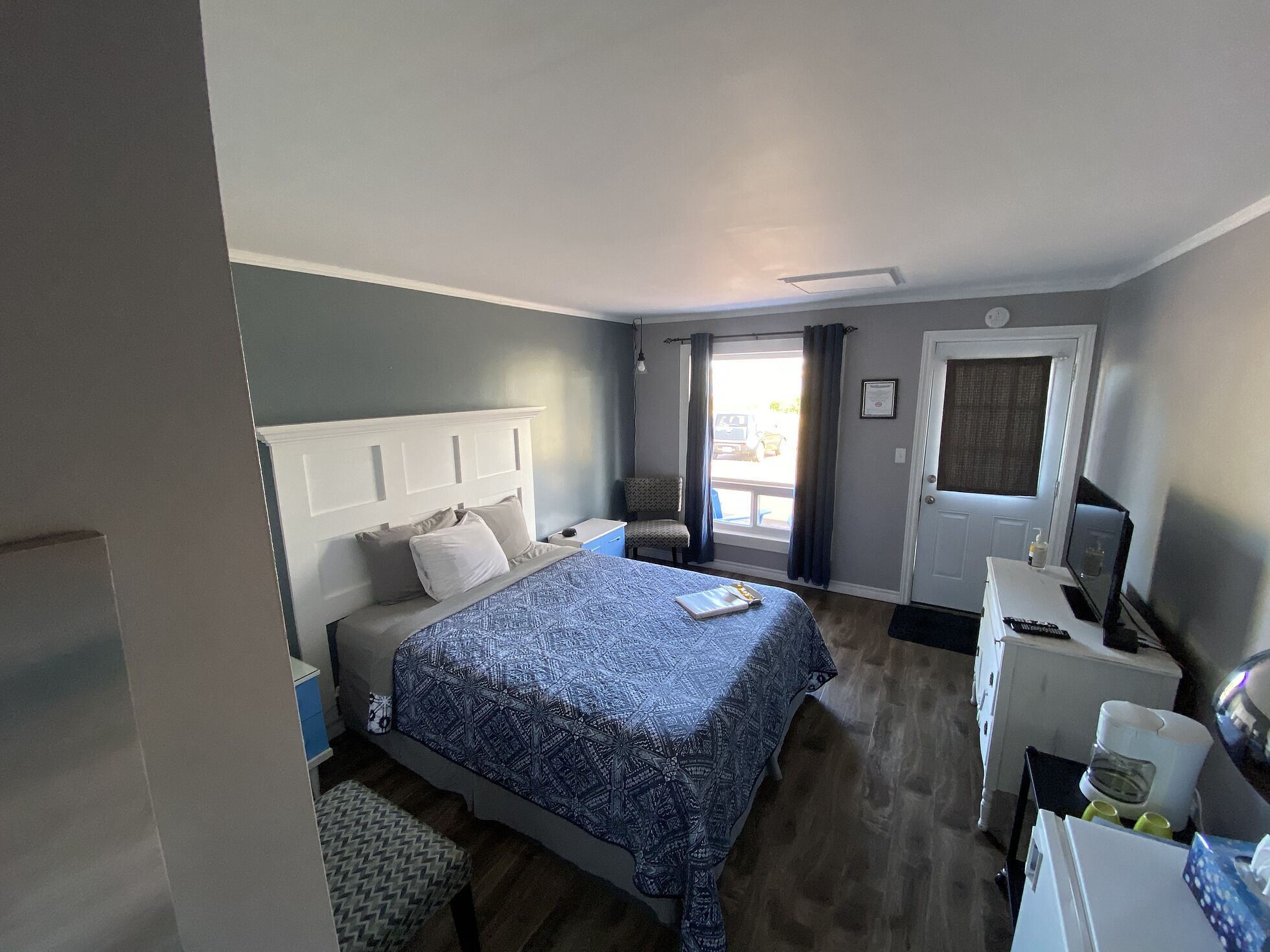 A bedroom with a bed, bedside table, chair, desk, and a door.