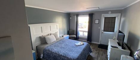 A bedroom with a bed, bedside table, chair, desk, and a door.
