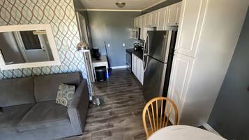 Un espacio habitable compacto con sofá, mesa de comedor, cocina con armarios y electrodomésticos, y una pared con diseño.
