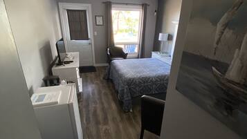 Une chambre d’hôtel compacte comprenant un lit, un bureau avec un ordinateur, une chaise, une fenêtre avec des rideaux et un tableau au mur.