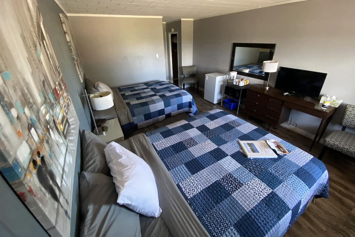 Una habitación de hotel con dos camas, un escritorio con televisor, un refrigerador pequeño y una silla.