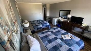 A hotel room with two beds, a desk with a television, a small refrigerator, and a chair.