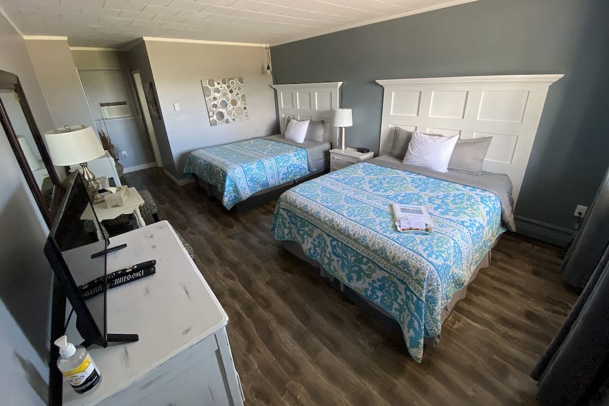 Habitación de hotel con dos camas, un escritorio con lámpara, un espejo y una obra de arte colgada en la pared.