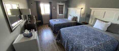A hotel room with two beds, a desk, a chair, a TV, and a window with curtains.